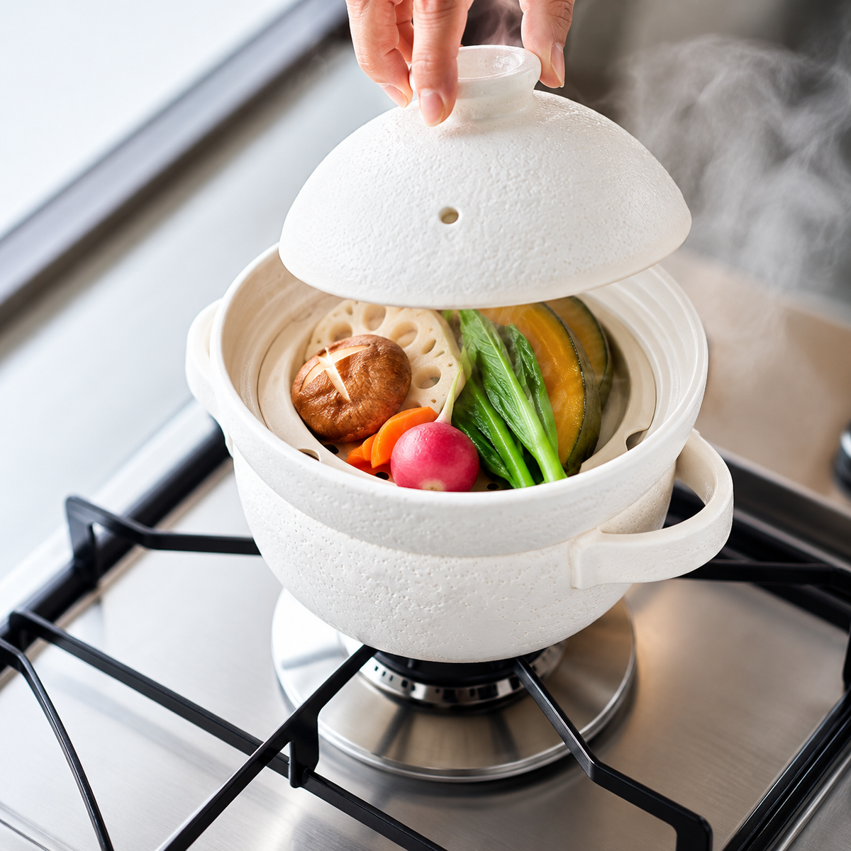 White INAHO ceramic steamer on a gas stove with assorted vegetables and the lid raised.