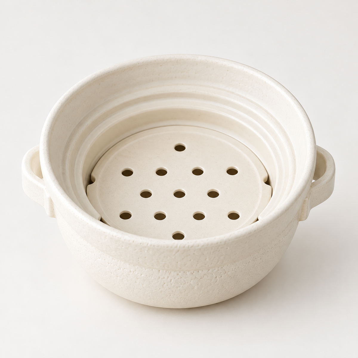 Close-up of the empty white ceramic steamer insert showing its round steam holes and rim.