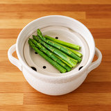 Green asparagus arranged on a perforated ceramic steaming insert inside the white INAHO donabe.