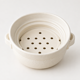 Close-up of the empty white ceramic steamer insert showing its round steam holes and rim.